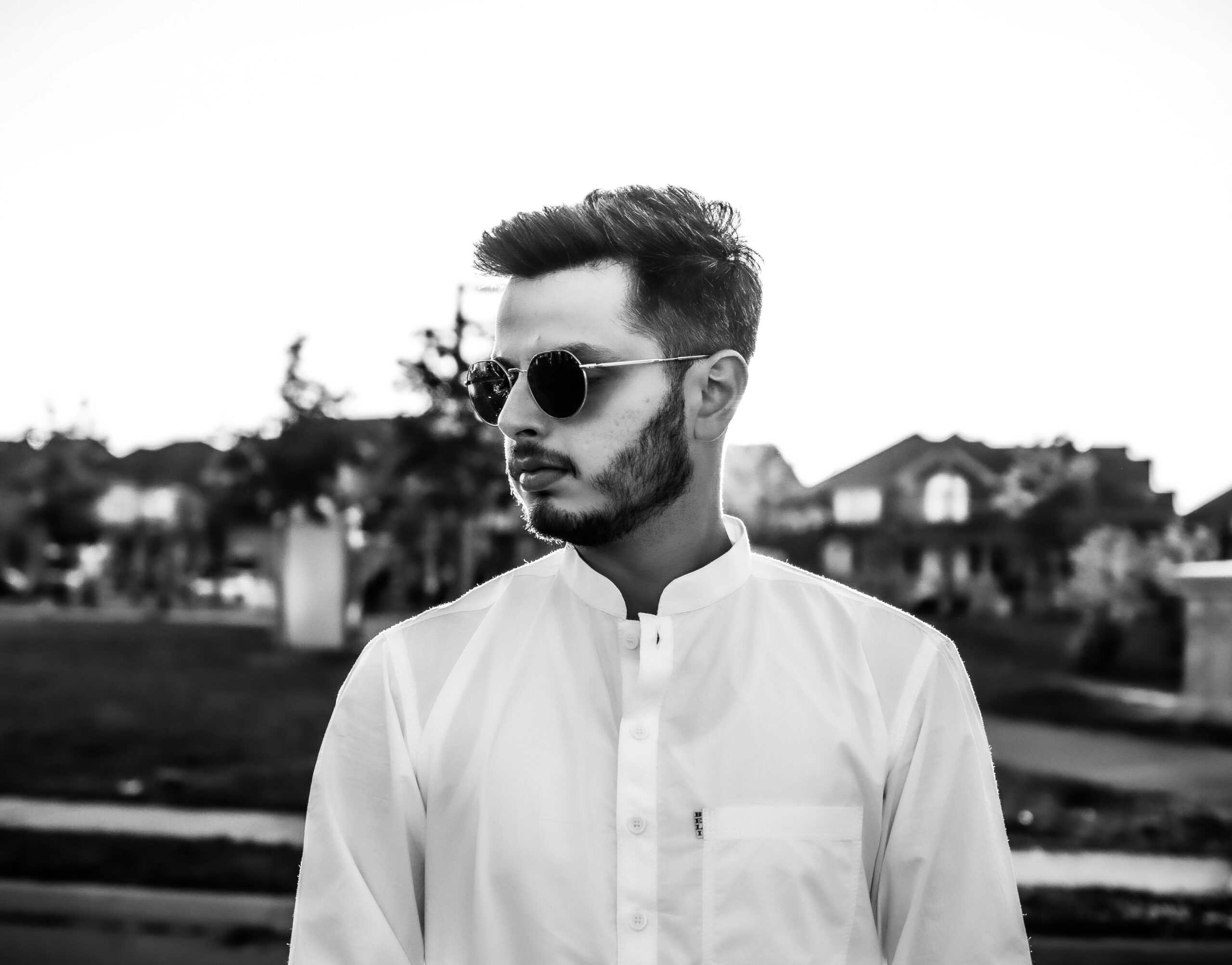 Bearded man in white shirt with sunglasses in a black and white outdoor setting.
